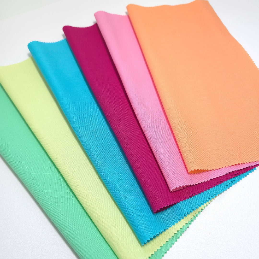Six squares of cotton fabric in assorted colors folded over and stacked in a fan pattern. 