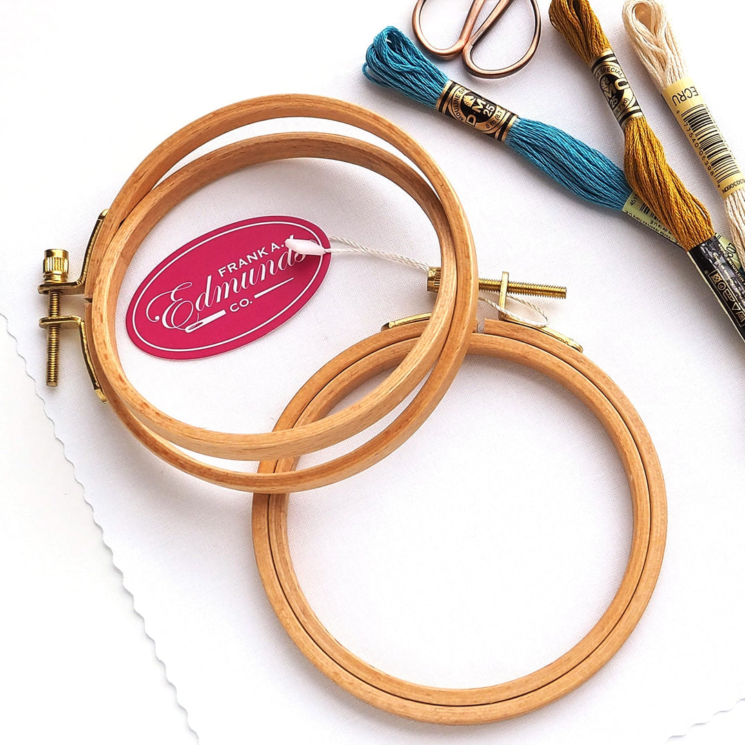 Two wood embroidery hoops next to several skeins of floss and a small scissors.