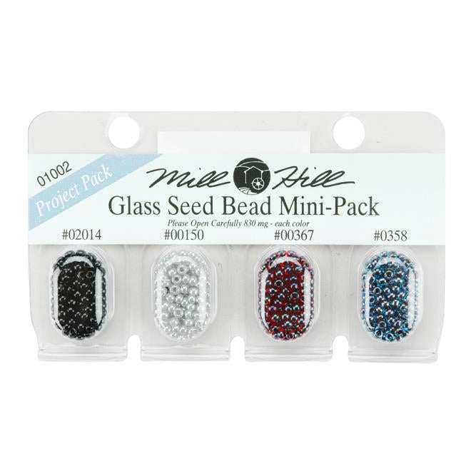 Mill Hill Glass Seed Bead Mini-Pack containing four small clear plastic blister packs filled with seed beads in black, gray, burgundy, and blue, on a white background.