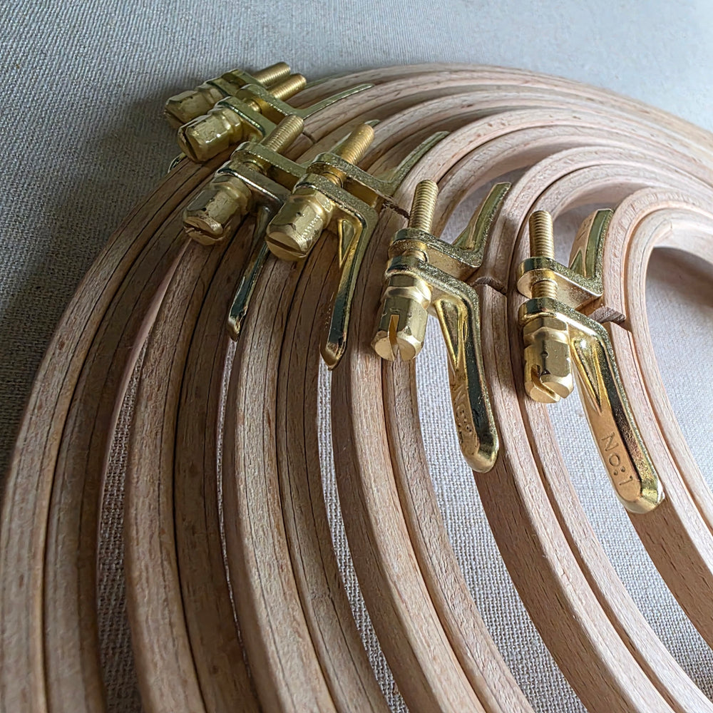 Set of wooden embroidery hoops with brass clamps on a light fabric background