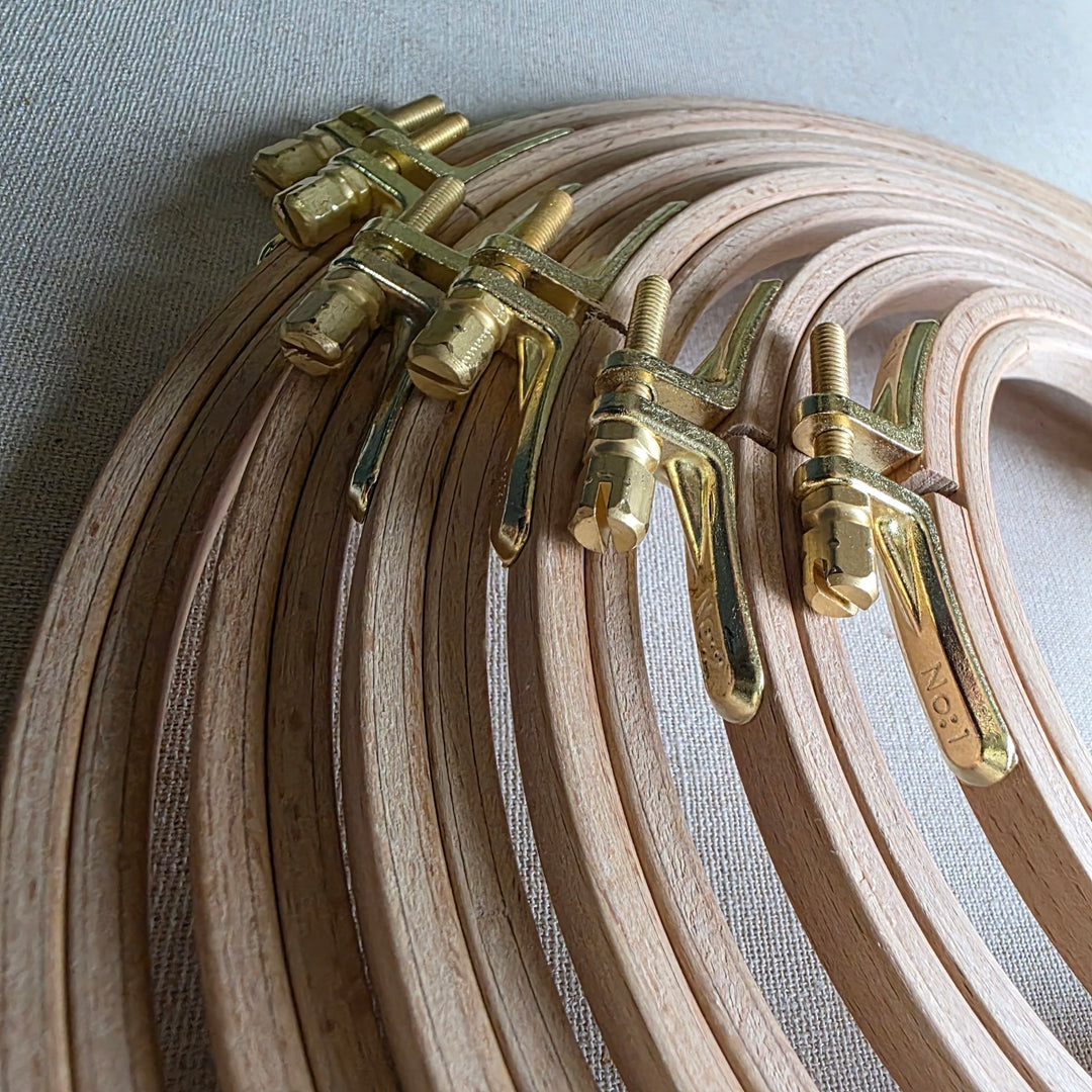 Set of wooden embroidery hoops with brass clamps on a light fabric background