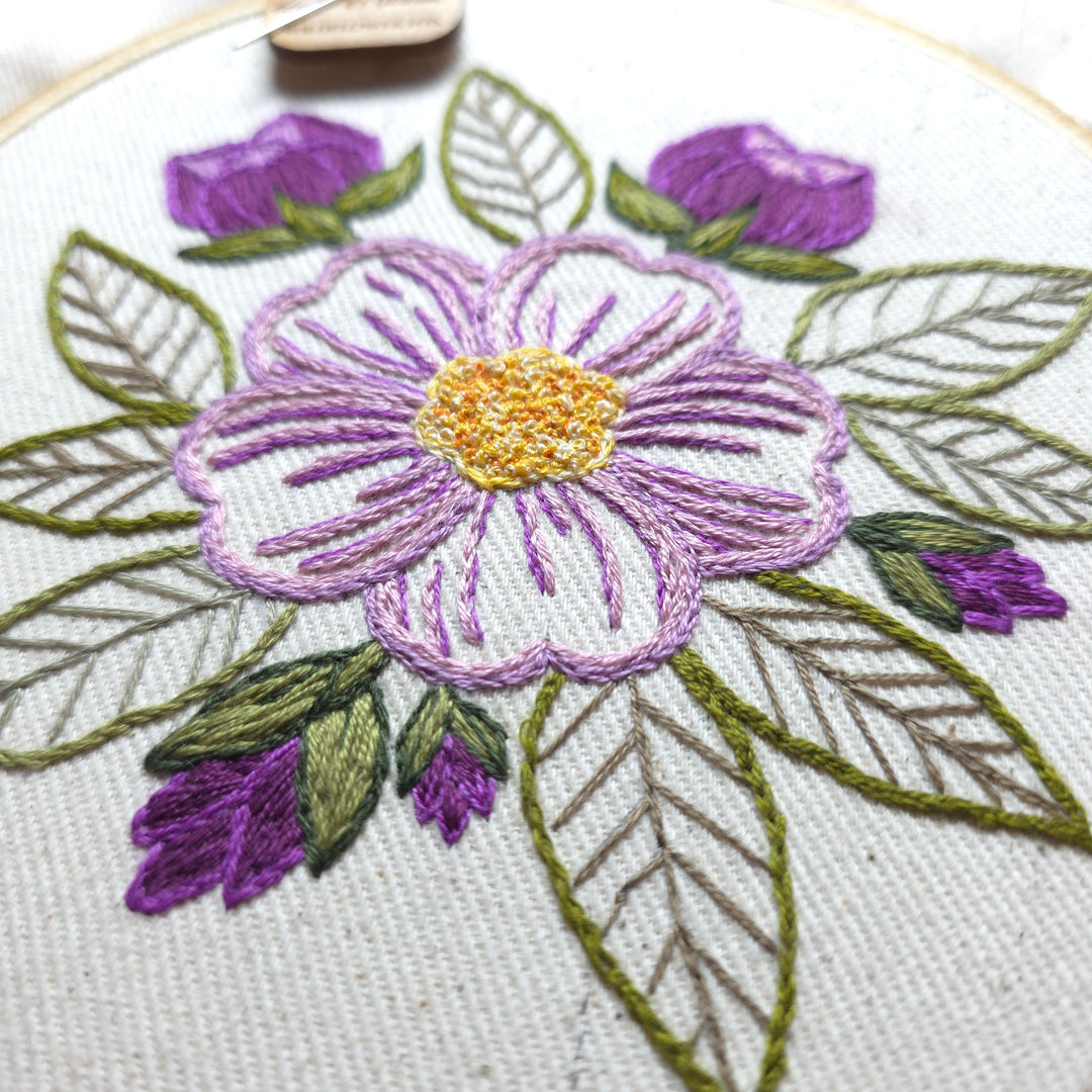Embroidered floral design with purple flowers and green leaves on a natural colored fabric